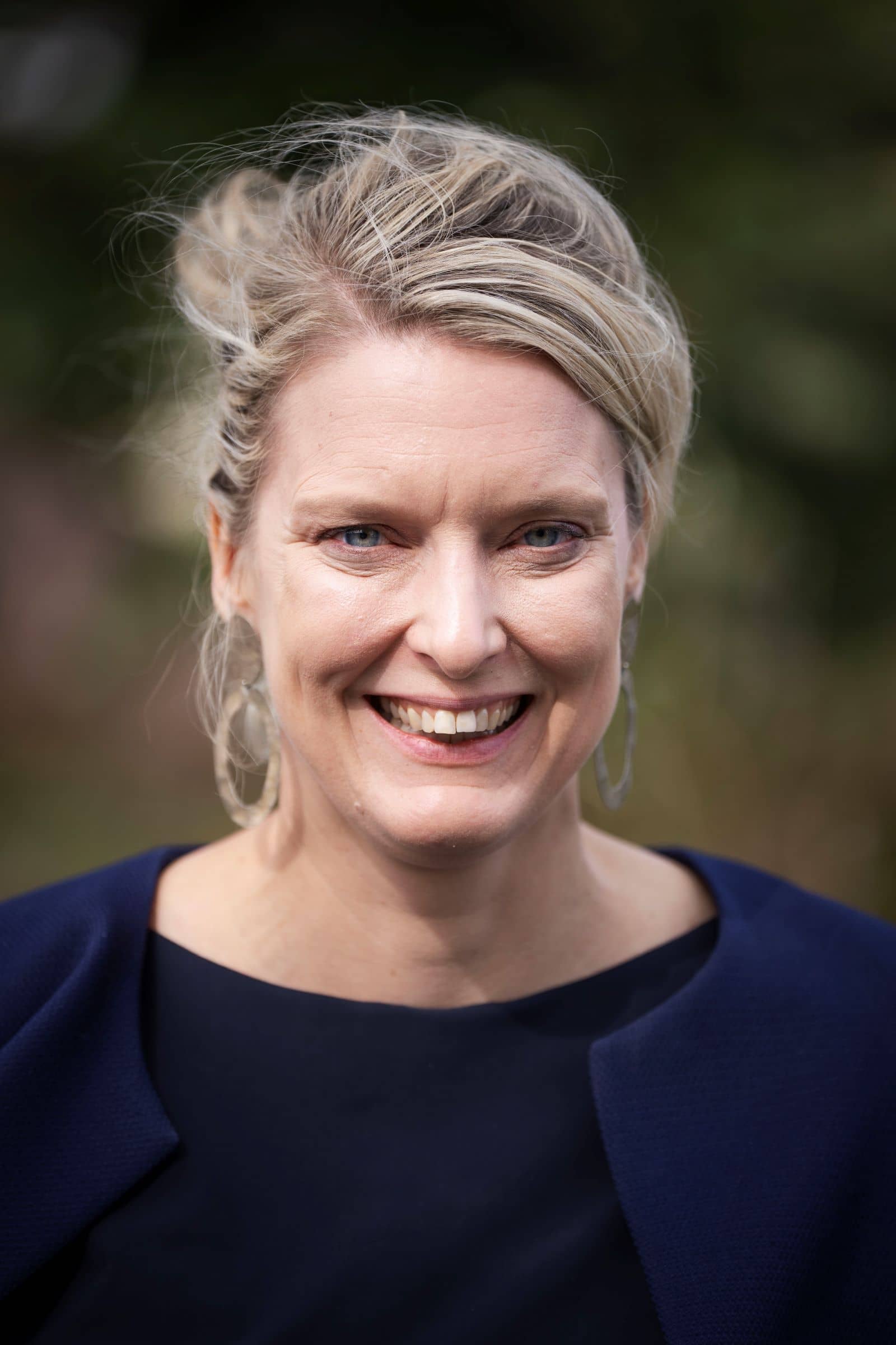 Een vrouw met opgestoken blond haar kijkt lachend naar de camera